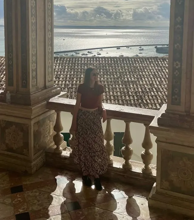 Gabriella numa janela em arco do museu, com telhados antigos e a baía ao fundo
